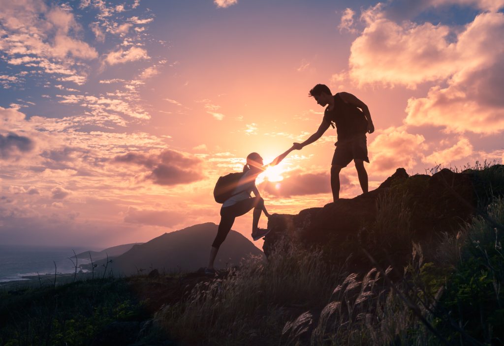 Two hikers climbing up mountain and one of them giving helping hand.